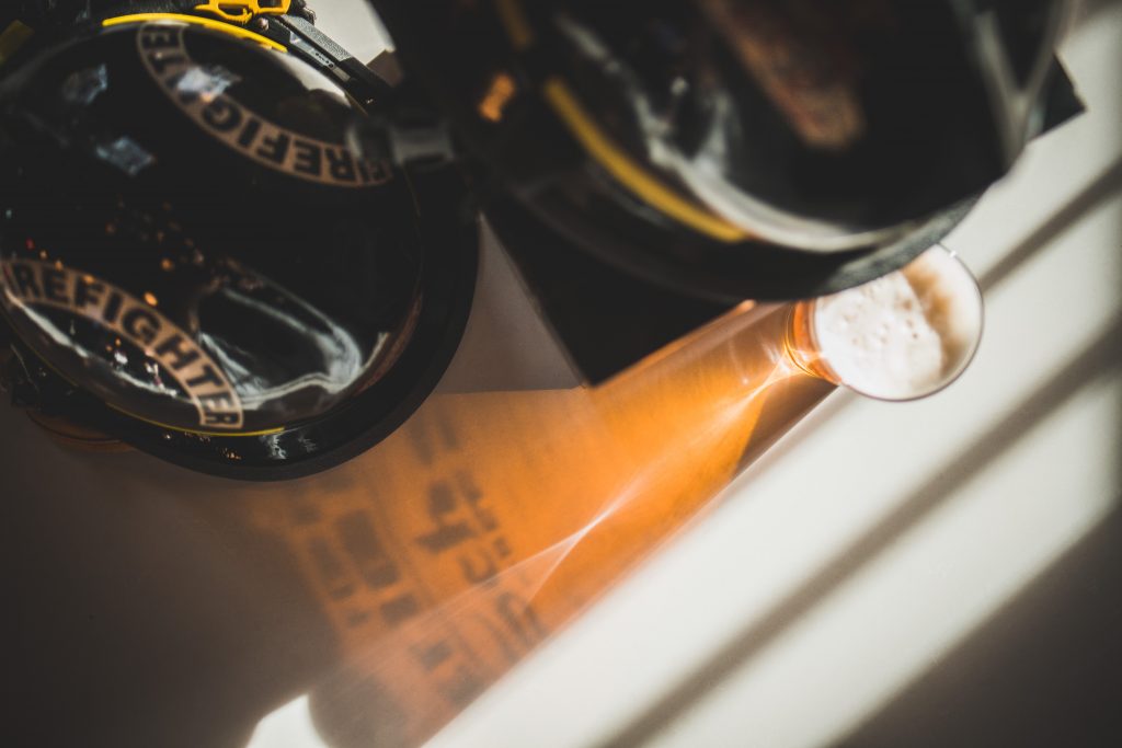 Overhead view of two firefighter helmets next to a full pint of beer
