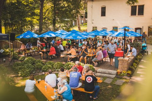 A large group sitting under patio umbrellas in the Schell's Brewery biergarten