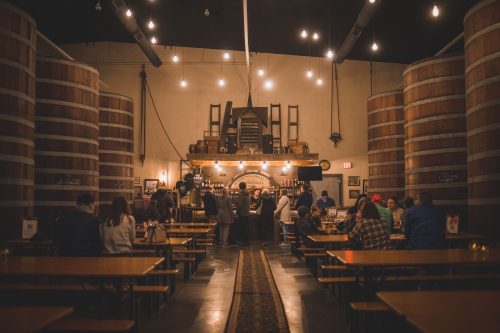 People ordering drinks at a bar and sitting at tables next to large wooden tanks in the Starkeller