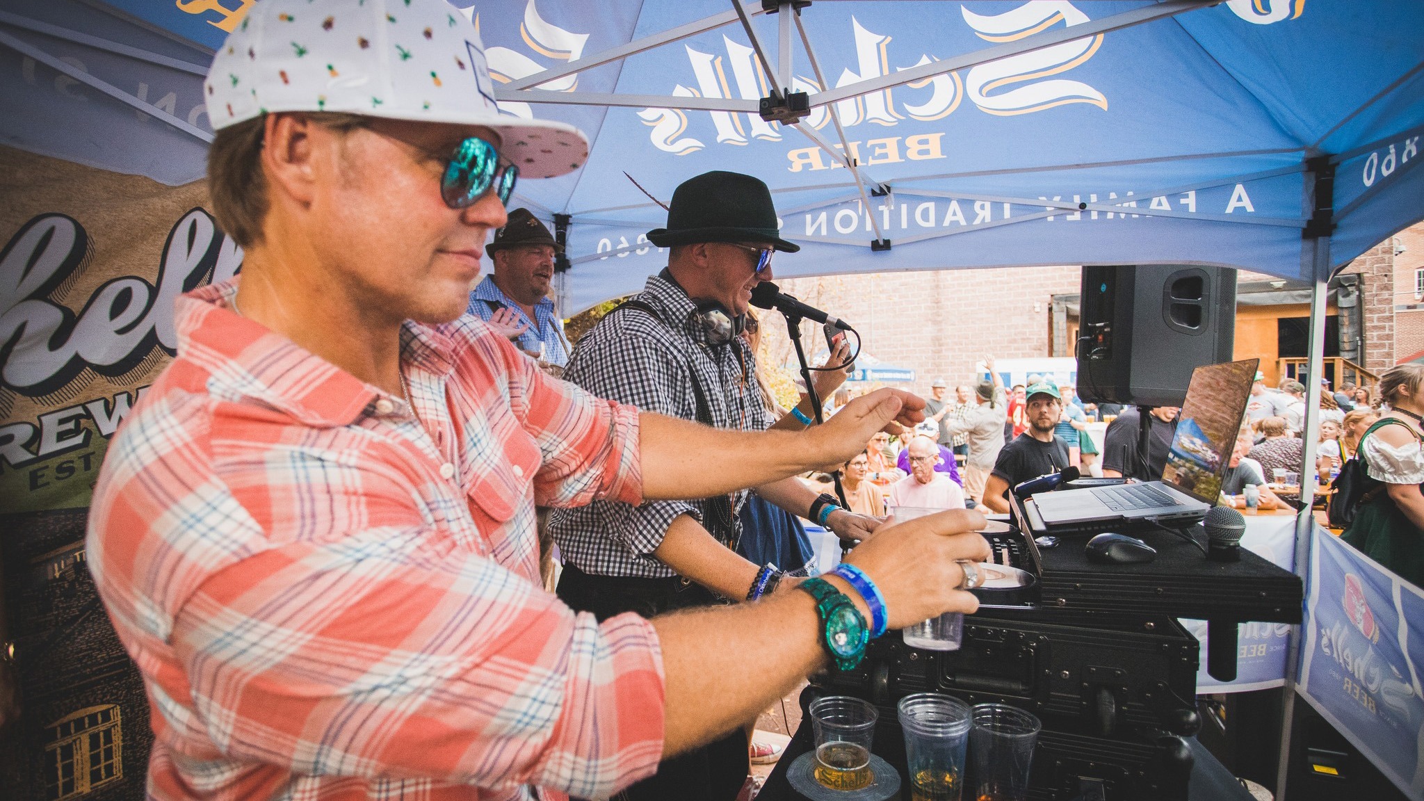 Two guys behind a DJ setup playing music for a crowd at Schell's Oktoberfest.
