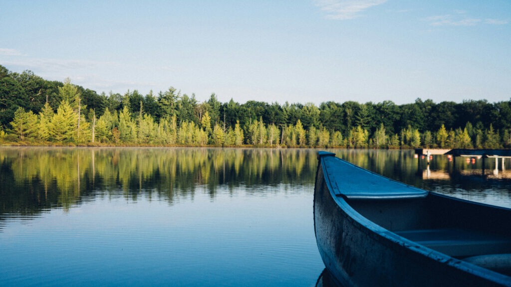 Empty canoe on a still lake with evergreen trees on the shoreline